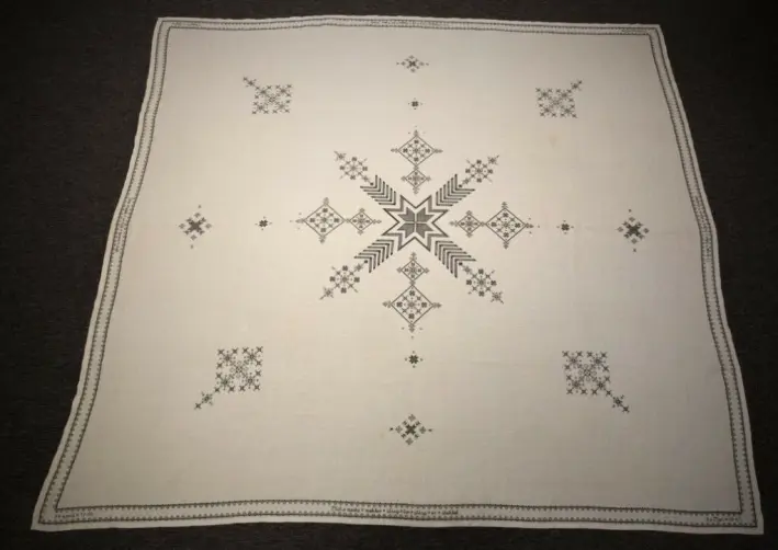 Caroline Moes duk. Borden har motsatte kors, som symboliserer de døde på begge sider. Andre referanser til krigen er også brodert inn. Duken har kaffeflekker fra feiringen av Hitlers død. Caroline Moes duk. Borden har motsatte kors, som symboliserer de døde på begge sider. Andre referanser til krigen er også brodert inn. Duken har kaffeflekker fra feiringen av Hitlers død.