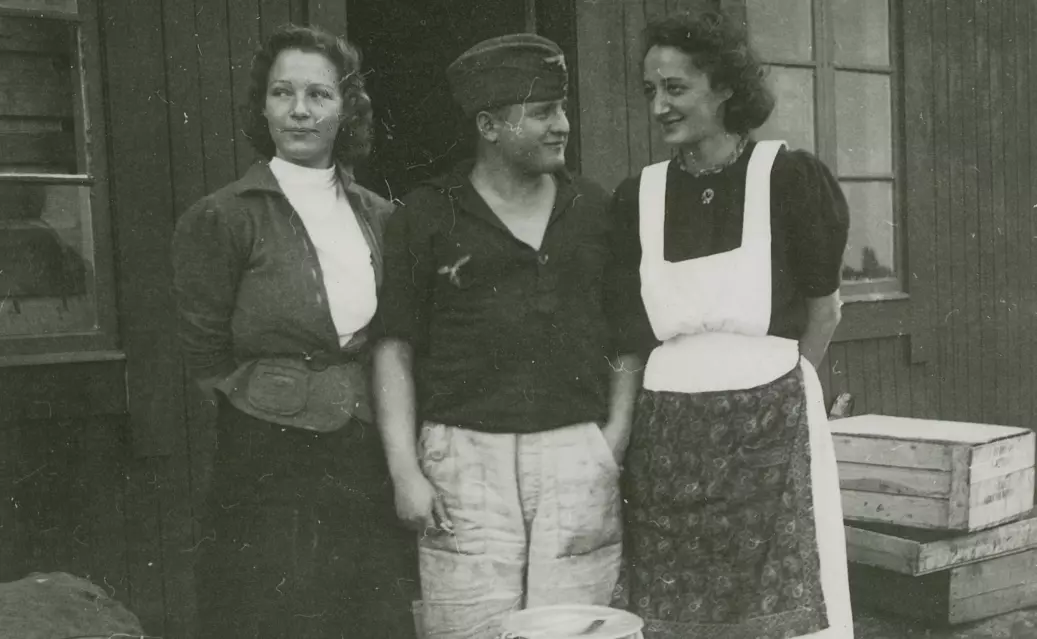 Bodø flyplass 1940. Luftwaffe-soldat i arbeidsuniform flankert av to norske kvinner, trolig kjøkkenhjelper.