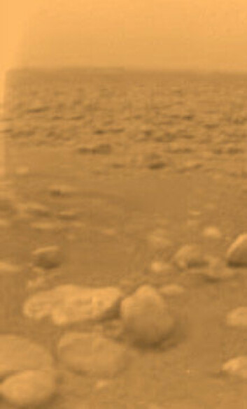 "Det første bildet fra overflaten på Titan. Steinene er mindre enn 15 centimeter i diameter og er rundt 85 centimeter borte fra kameraet. Bildet er tatt av landingsproben Huygens i januar 2005."