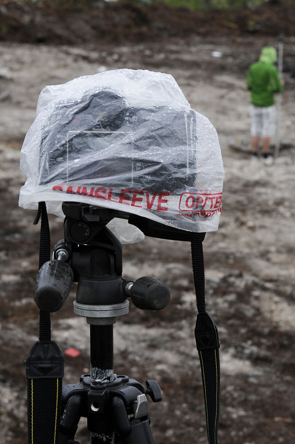Her ser du timelapsekameraet i aksjon, godt pakket inn for å beskytte mot regnvær. Det dokumenterer en av arkeologene som måler inn såkalte topopunkter, eller topografiske punkter med totalstasjon. (Foto: Raymon S. Hansen/Tromsø Museum)