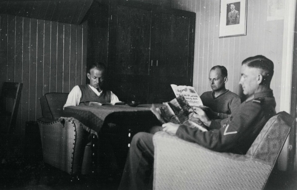 Soldater i både sivilt og uniform leser i et rekvirert hus i Narvik under okkupasjonen.