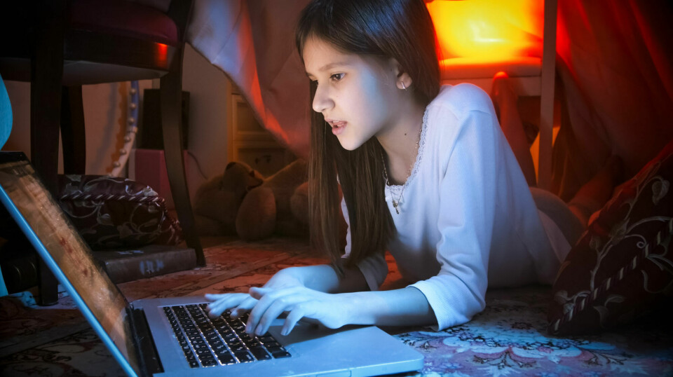 Ung jente skriver på datamaskin i dunkelt belyst rom.