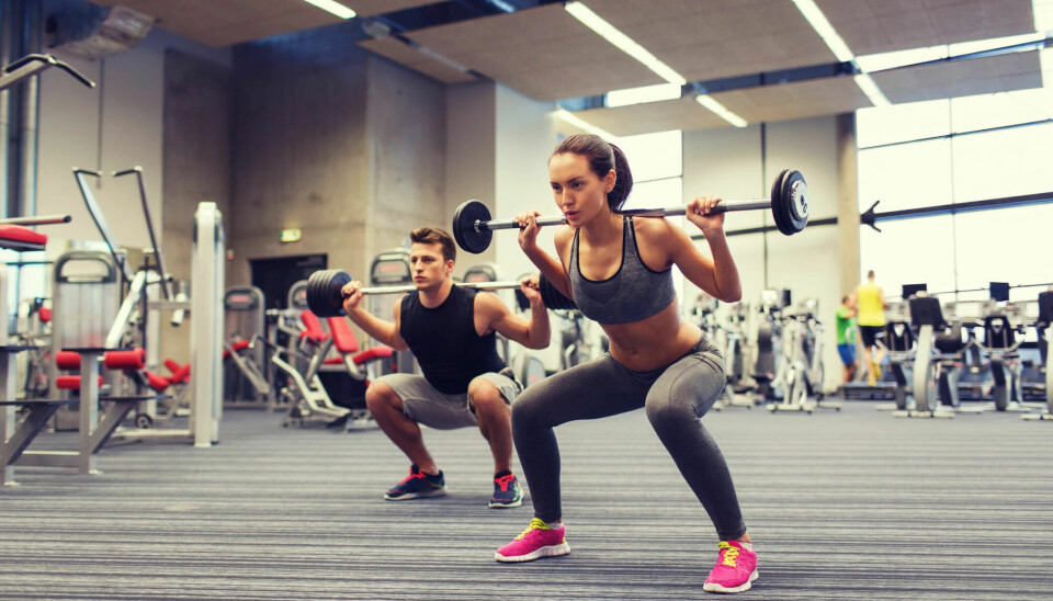 A woman and a man doing weighted squats in a gym.