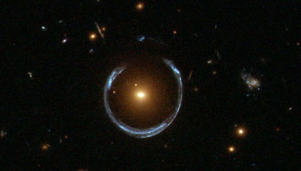 Dette er en ekstrem gravitasjonslinse. Det blå lyset rundt det røde i midten er en galakse langt bak. Gravitasjonen bøyer og vrir lyset til en ring rundt den røde galaksen.