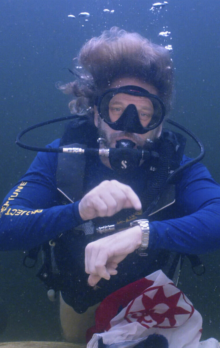 In this photo provided by the Florida Keys News Bureau, diving explorer and medical researcher Dr. Joseph Dituri points to his watch Friday, June 9, 2023, indicating that it is time to surface after spending 100 days in the Jules' Undersea Lodge marine habitat at the bottom of a Key Largo, Fla., lagoon. Dituri broke the previous 73-day record for underwater human habitation at ambient pressure, undertook medical and marine science research and interacted online with more than 5,500 students during his Project Neptune 100 mission organized by the Marine Resources Development Foundation. (Mariano Lorde/Florida Keys News Bureau via AP)