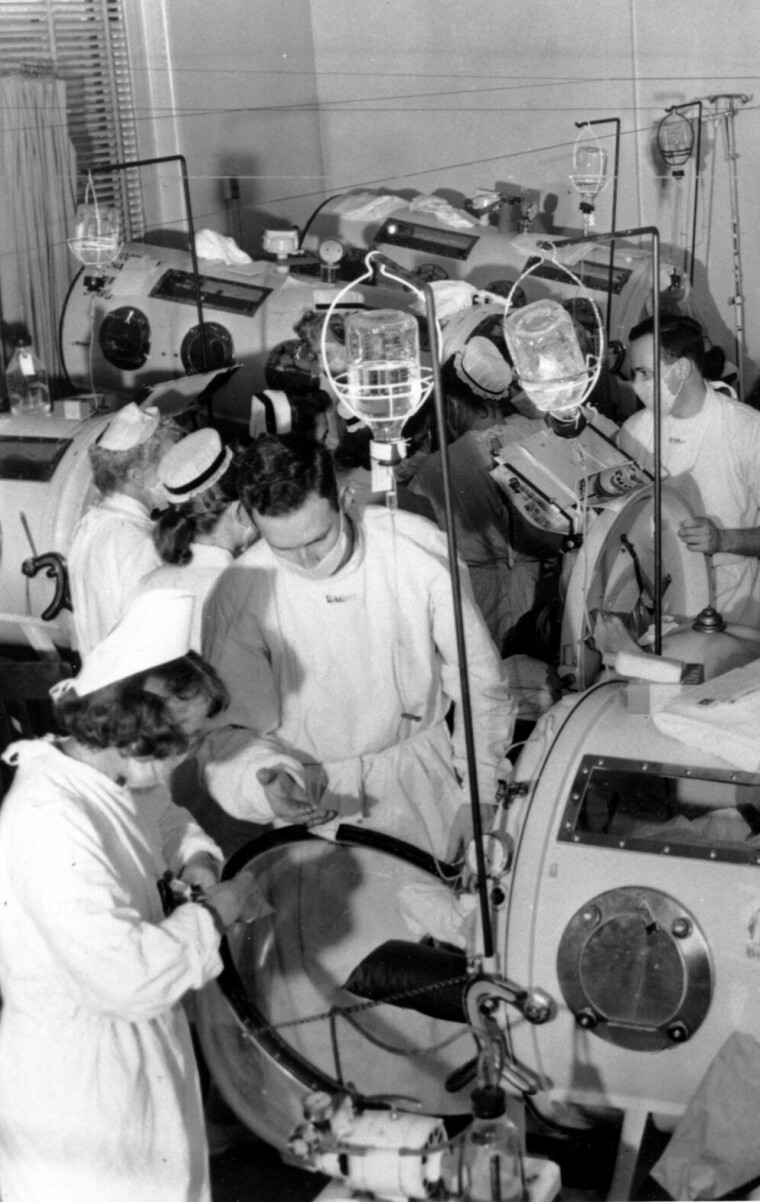 This is a scene in the emergency polio ward at Haynes Memorial Hospital in Boston, Ma. on Aug. 16, 1955. The city's polio epidemic hit a high of 480 cases. The critical patients are lined up close together in iron lung respirators so that a team of doctors and nurses can give fast emergency treatment as needed. (AP Photo)
