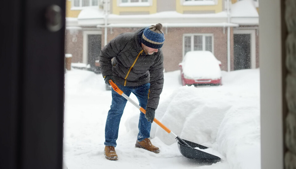Mann måker snø foran leiligheter i by.For mange har det blitt vanskeligere å betale boutgiftene.