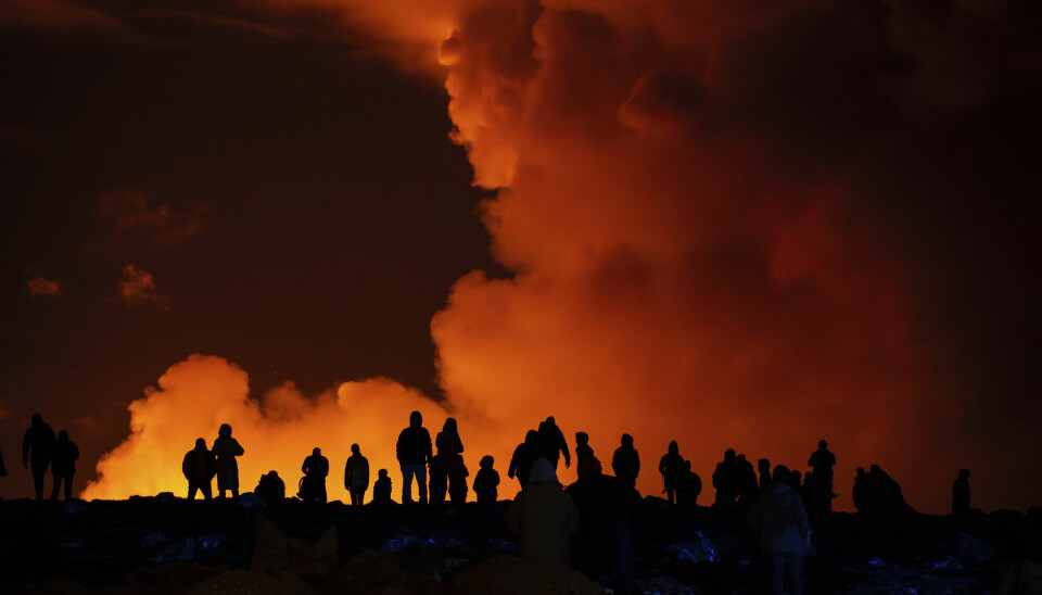 Menneskene står i mørket og ses som svarte silhuetter mot den oransje røykskyen.
