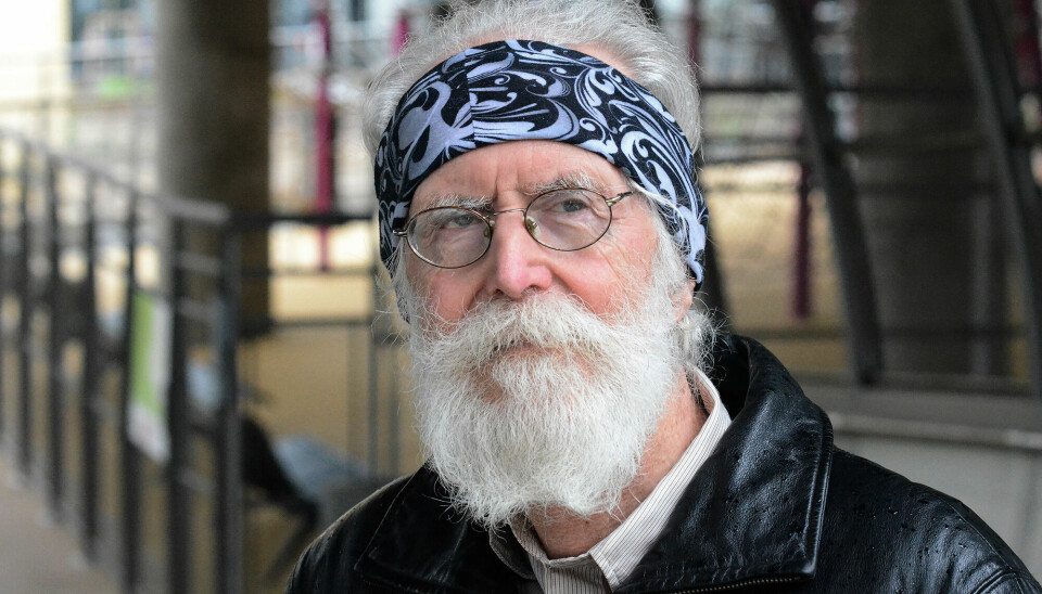 Nærbilde av en alvorlig Michel Talagrand i sort skinnjakke med hvitt skjegg, briller og et mønstret halstørkle rundt hodet.