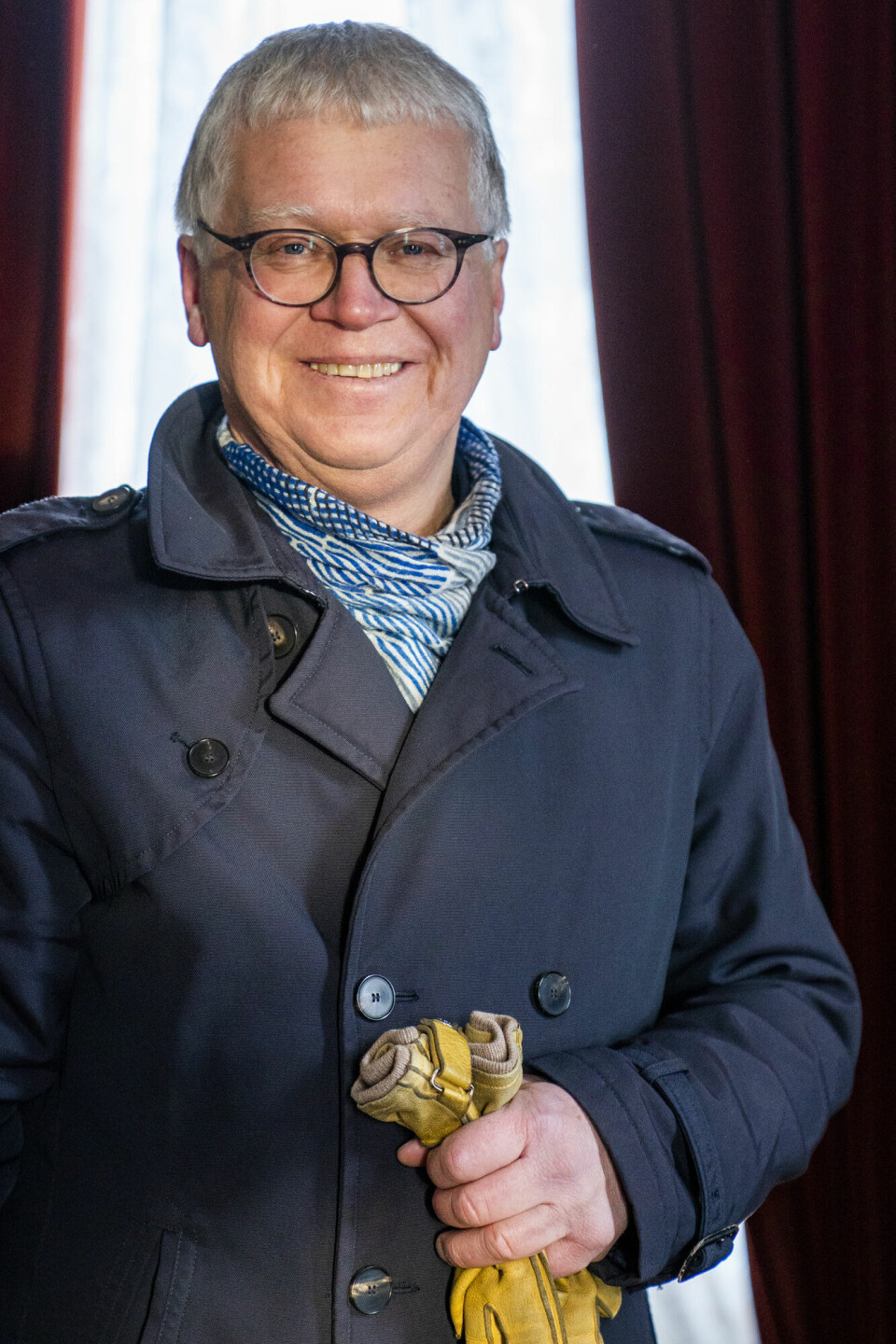 Konservator Geir Thomas Risåsen. Han har runde briller og mørkeblå frakk. I venstre hånd holder han et par gule hansker.