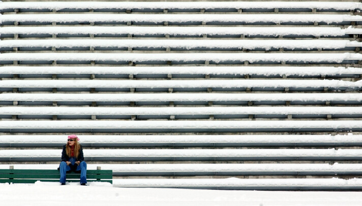 En kvinne sitter alene nede i venstre hjørne av bildet. Bak henne er det 16 rader med sitteplasser dekket av snø.