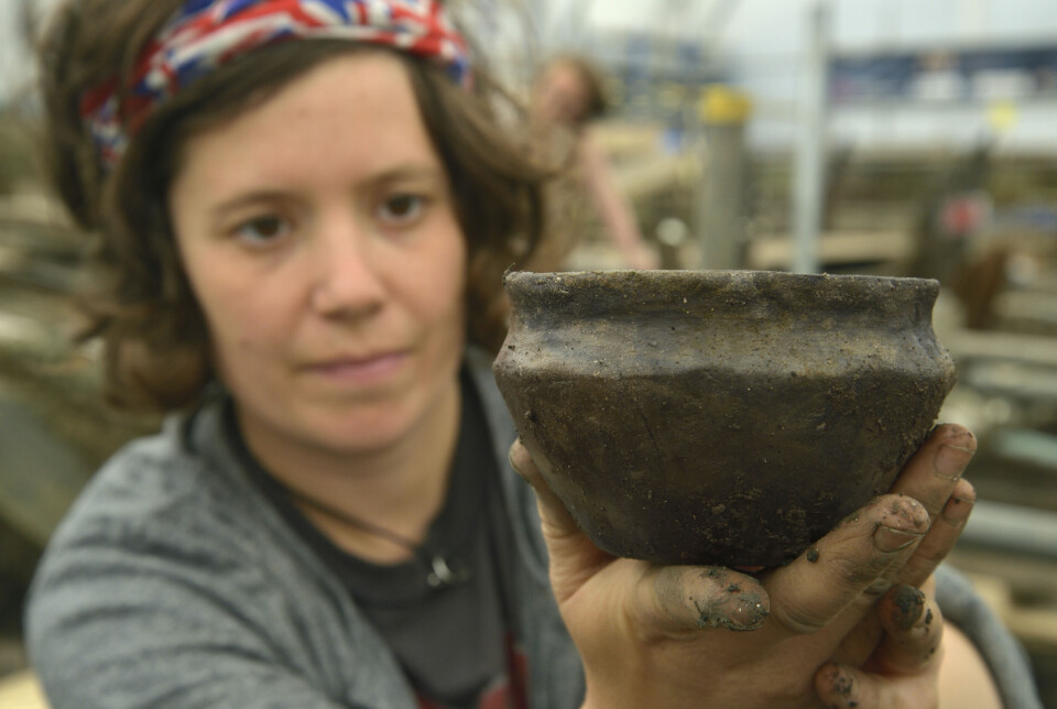 En ung kvinnelig forsker holder fram en hel bolle av keramikk. Hendene hennes og bollen er brune av jord.