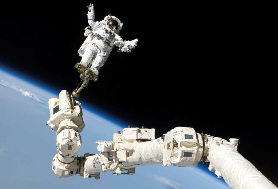 Astronaut og robotarm i verdensrommet rundt jorden.