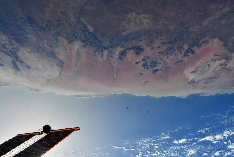 Ørkenen er opp ned øverst i bildet. Under er det blå himmel, og vi ser litt av romstasjonen.