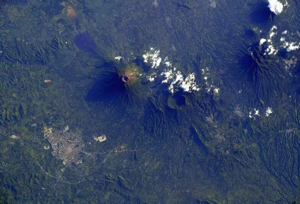 Vulkanens gapende hull er midt i bildet. Fargene på bildet er i grønt og blått, og det er fjellandskap.