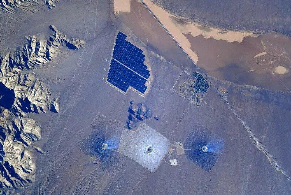 Brunt ørkenlandskap. Til venstre er det fjell. Midt i bildet er det noe som ser ut som solpaneler. Under er det tre rundinger som lyser blått.