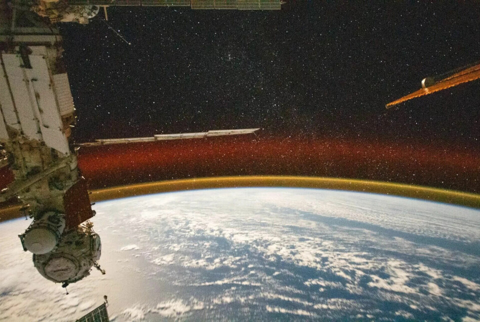 Nedre halvdel av bildet viser jordkloden i blått med hvite skyer på. Over den lyser et rødt lys opp den svarte nattehimmelen. Til venstre er det et hvitt instrument.