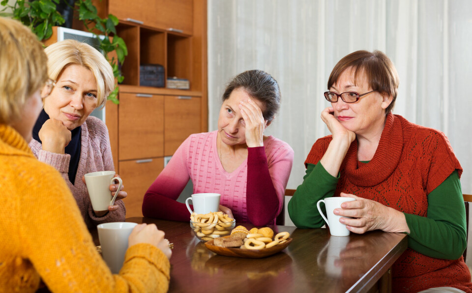 Fire middelaldrende kvinner sitter og prater rundt et bord med kaker på bordet og kaffekopper i hendene. Det er én av dem som ser ut til å prate mest.