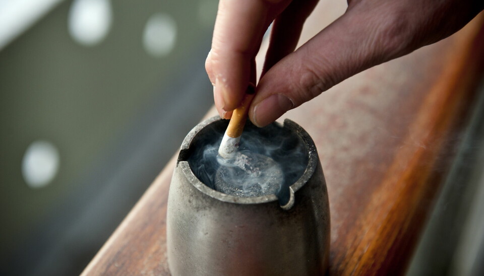 Hånd som stumper sigarett i et metallaskebeger.