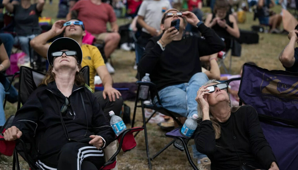 Flere mennesker sitter i sammenleggbare tur-stoler og ser opp mot himmelen med solbriller på.