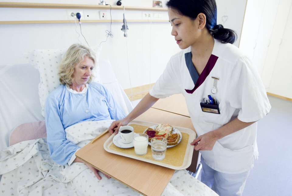 Kvinnelig pasient i sykehusseng får servert mat av sykepleier.