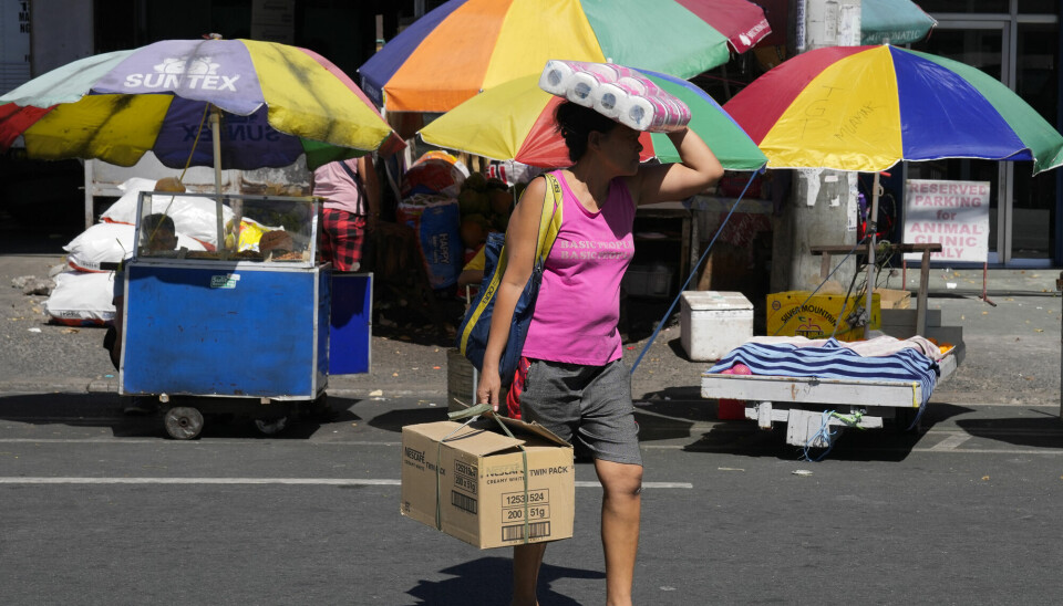 Kvinne i rosa singlet og grå shorts holder en stor pappeske i den ene hånda. Med den andre holder hun en pakke dopapir over hodet som beskyttelse mot sola.