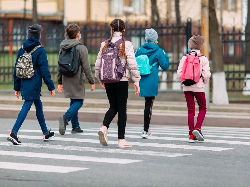 Fem jenter med ryggsekker og klær i forskjellige farger krysser en vei via en fotgjengerovergang. De er fotografert bakfra.