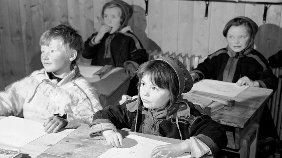 Black and white photo of four young children at sat at their desks at school