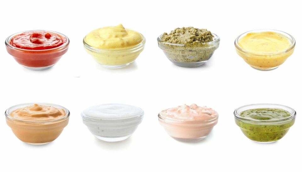 Mange små glasskåler med ulike sauser står på rekker med hvit bakgrunn.
