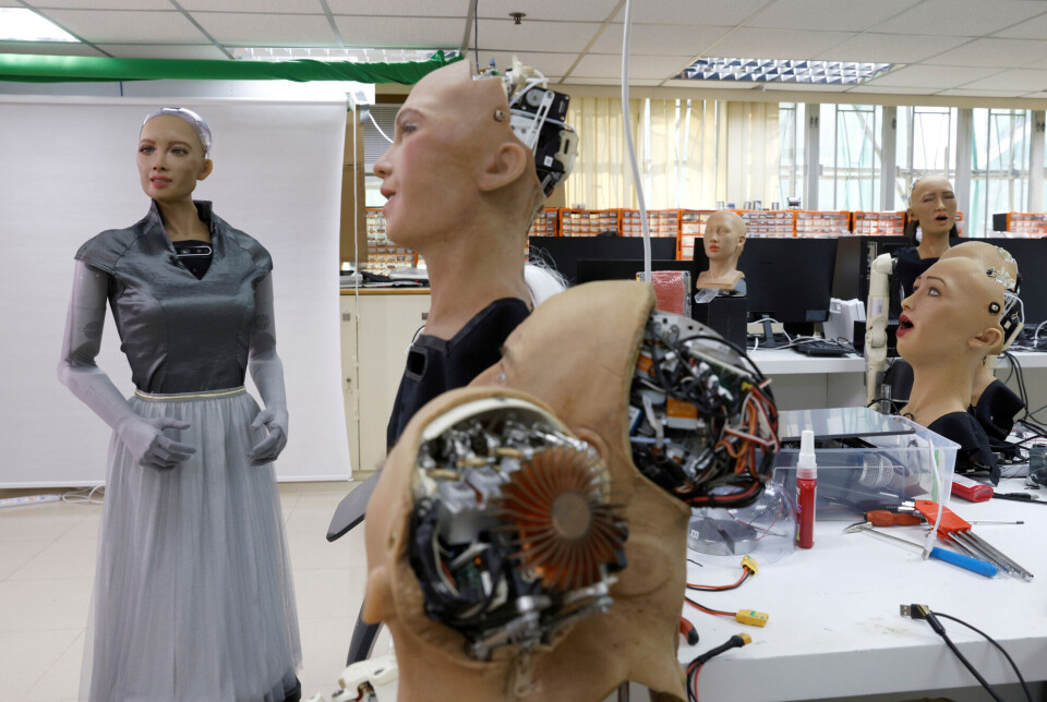 Roboten Sofia er svært menneskelignende. Den lages av Hanson Robotics. Bildet er fra deres lab i Hong Kong i 2021. En menneskelignende robot står på siden. Flere robot-hoder av samme type står ved siden av.
