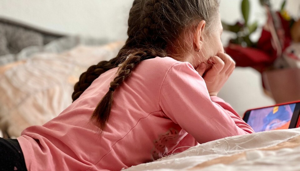 En ung jente ligger på magen, hodet er støttet opp av hendene mens hun ser på en mobilskjerm.