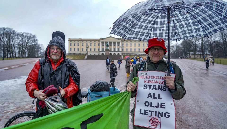 Bilde av to eldre klimaaktivister foran slottet. Den ene mannen står med en paraply og rundt halsen henger et stort skilt som viser at han tilhører gruppen Besteforeldre for Klimaaksjonen. På skiltet står det Stans all oljeleting. Han holder også i et banner, men man ser kun enden.