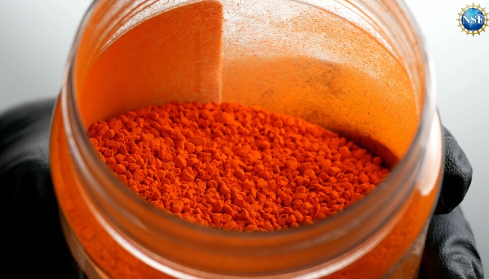 Slik ser tartrazin ut før du blander det med vann. Det er lov til å bruke litt av dette fargestoffet i mat. En hånd med sort hanske holder et glass med knall oransje pulver.