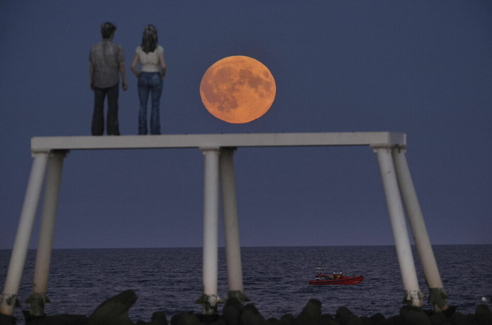 Supermånen var synlig over «The Couple»-skulpturen ved Newbiggin-by-the-Sea i Northumberland i England tirsdag kveld 17. september 2024. Statue av en mann og en kvinne som skuer ut over havet. Guloransje fullmåne i bakgrunnen.