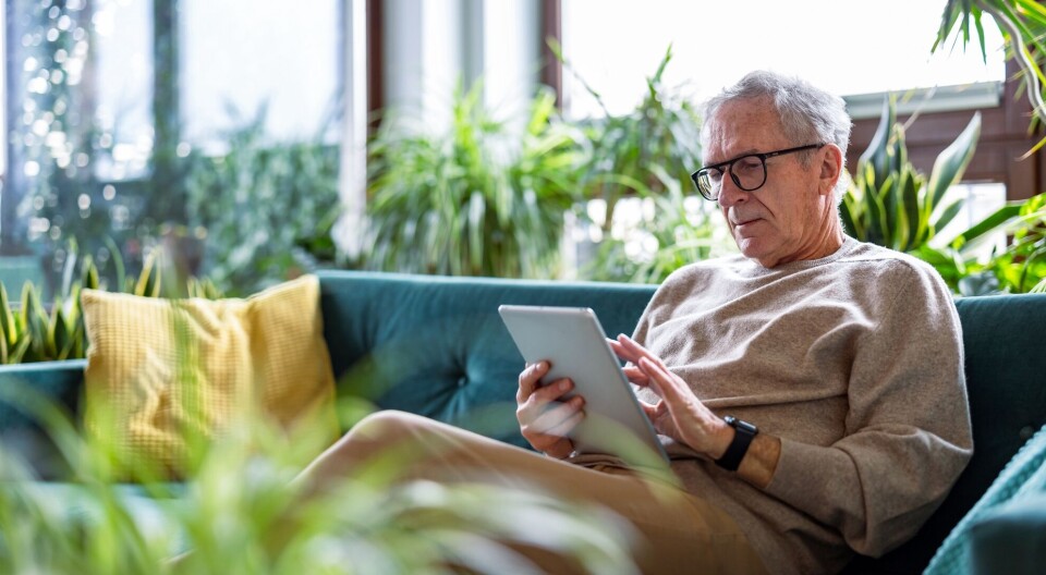 Mange fysioterapeuter følger opp pasientene digitalt. Mann i sofa med nettbrett