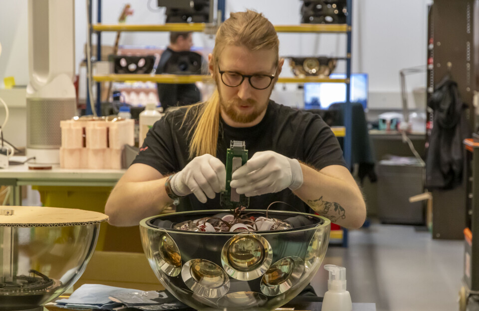 En forsker jobber med en liten bit av utstyret som nå har oppdaget den mest energirike partikkelen vi noen gang har registrert. En forsker jobber med elektronikk inne i en gjennomsiktig halvkule på et bord. Inni halvkula sitter mange kamera med linsene utover mot glasset.