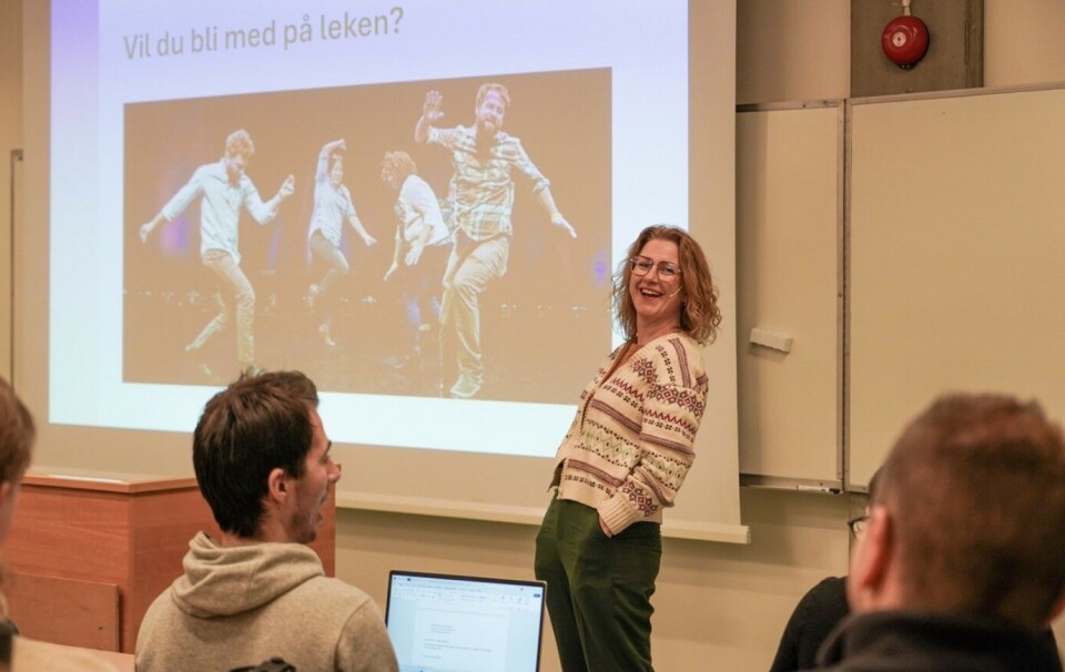 Helene Abrahamsen, improvisatør, skuespiller og psykolog skapte god stemning i auditorium E før hun ba om frivillige opp til seg for noen øvelser. Kvinne ler foran tavle