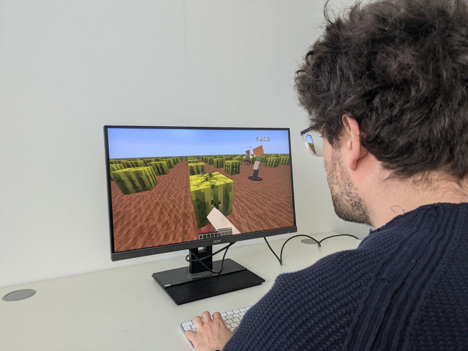 Forskere har brukt Minecraft for å undersøke hvordan mennesker lærer seg sosiale ferdigheter i realistiske, virtuelle omgivelser. Mann sett bakfra spiller Minecraft. Skjermen hans viser brunt landskap med grønne, firkantede blokker.