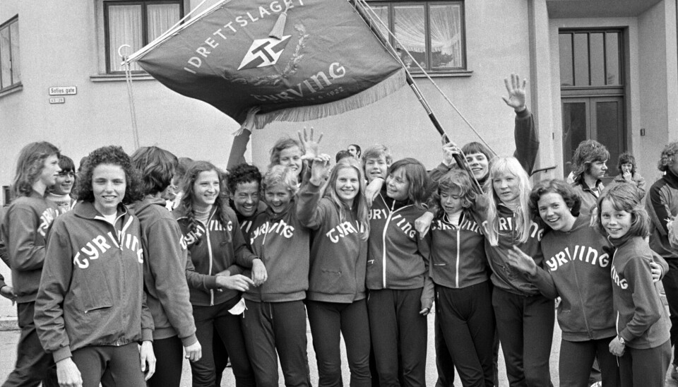 Gerd von der Lippe (lener seg frem som nummer seks fra venstre) og resten av vinnerlaget i kvinneklassen i 1975. Tre år tidligere løp hun under navnet «Øyvind Foss». Unge kvinner med Tyrving-gensere veiver med et flagg hvor det står «Idrettslaget Tyrving».