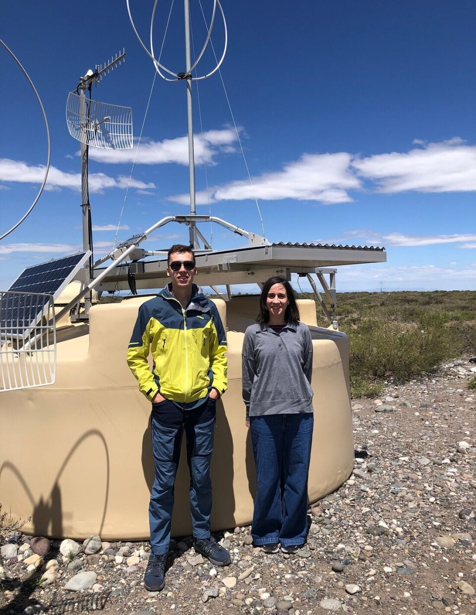 Domenik Ehlert og Foteini Oikonomou foran en av de 1.600 overflatedetektorene som hører til Pierre Auger Ultra-high Energy Cosmic Ray Observatory i Malargue i Argentina. To personer