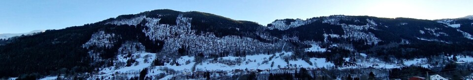 Ei typisk vestlandsk li med mørke felt av granskog, kulturmark som her er snødekt, og lauvskog innimellom.