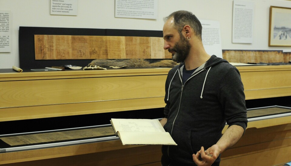 Federico Aurora med en bok med publiserte papyruser. Federico Aurora står foran en skuff og holder en bok.