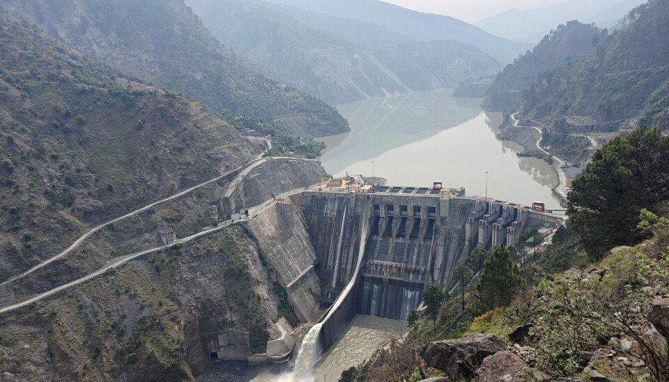 Den indiske demningen Baglihar Dam ligger ved elva Chenab i Jammu og Kashmir. Demning med brunt vann foran og bak, omgitt av fjell.