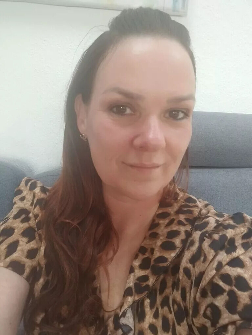 For Helle Hansen er ChatGPT som en psykolog. Er det noe hun vil diskutere, spesielt om datteren sin, bruker hun den. Og hun er imponert over svarene den gir. En kvinne med langt brunt hår og lys hud sitter i en grå sofa og smiler lett. Hun har på seg en topp med leopardmønster og små øredobber, og i bakgrunnen sees en lys vegg.