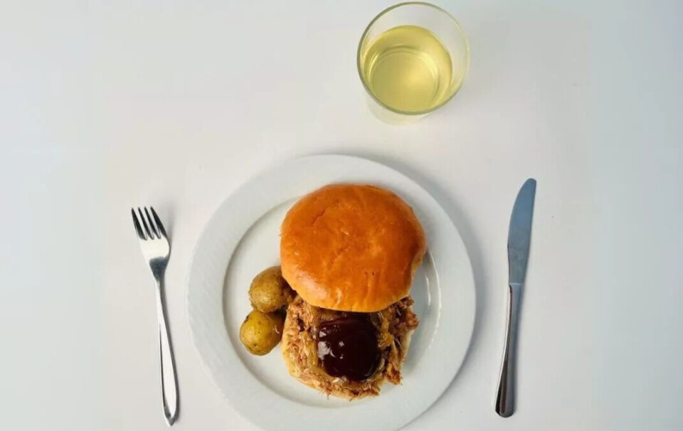 En av de ultraprosesserte middagene besto av pulled pork med ferdigkjøpt karamellisert løk og barbecuesaus på brioche, ferdigbakte poteter og limonade. Rent bilde med hvit bakgrunn viser maten på en hvit tallerken med kniv og gaffel og et glass med lysegult innhold.
