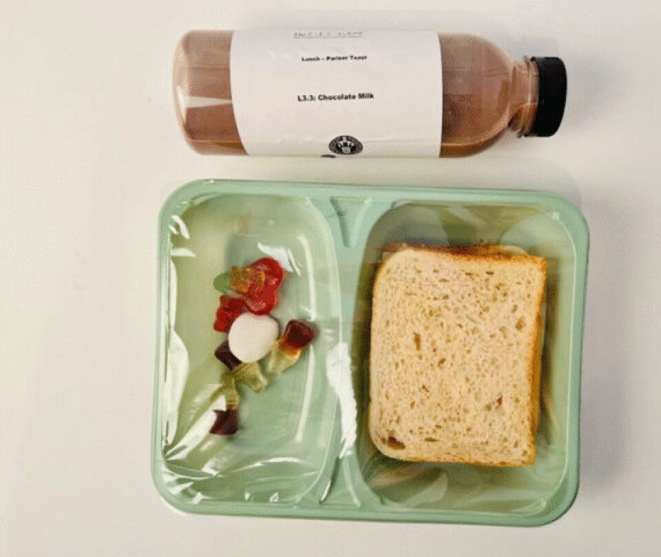 Ultraprosessert lunsj med et smørbrød med skinke og ost, godteri og sjokolademelk. Stilisert bilde på hvit bakgrunn av en flaske sjokomelk som ligger øverst og under: en grønn plastboks med gummigodteri til venstre og brødskive til høyre.
