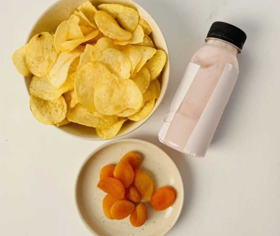 Ultraprosessert kosemat: Potetgull med smak av rømme og løk, tørkede aprikoser og en bringebærproteindrikk. Stilisert bilde på hvit bakgrunn av en hvit bolle med potetgull, en mindre, hvit asjett med tørkede aprikoser og en liggende, liten plastflaske med lyserosa innhold.