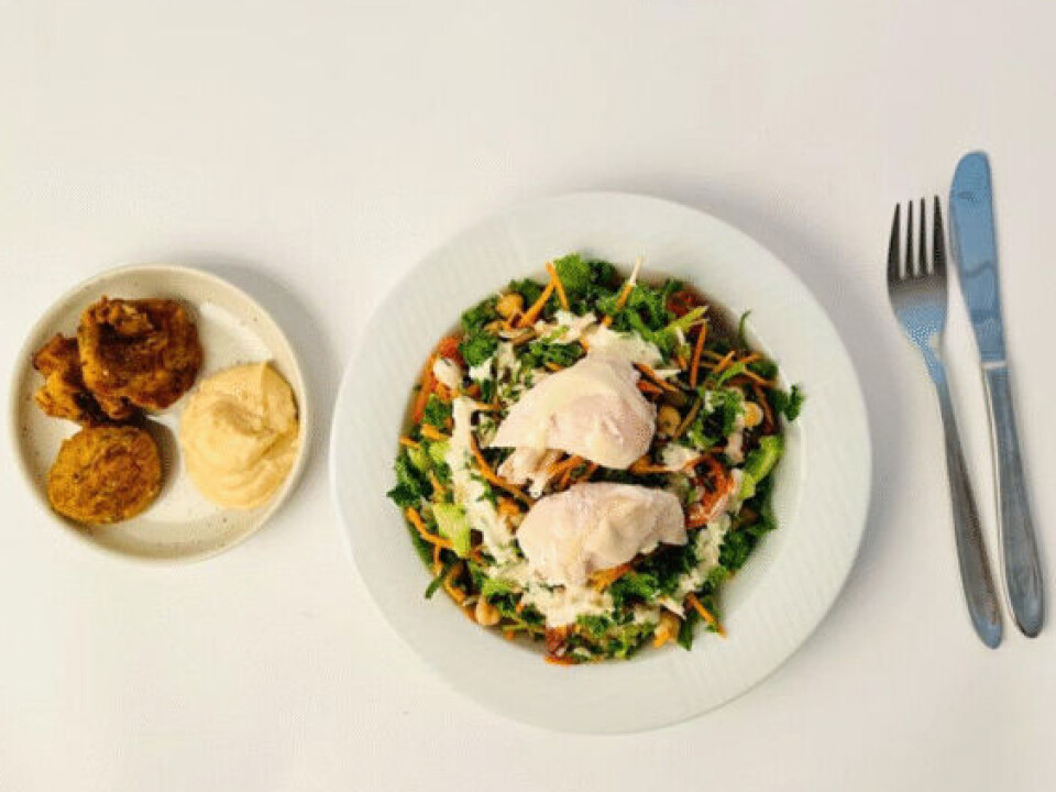 Minimalt prosessert lunsj: Quinoa- og spinat-salat, poteter, laks, rugbrød og appelsindressing. Stilisert bilde med hvit bakgrunn. Til venstre en hvit tallerken med ti poteter og et stykke laksefilet som ligger oppå spinat, quinoa og tomater. Til høyre en liten, hvit asjett med to skiver rugbrød og en liten glasskål med gulhvit saus. Kniv og gaffel ved siden av.