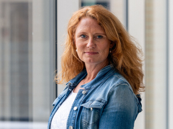 Pernille Rieker leder ARENA Senter for europastudier ved Universitetet i Oslo. Kvinne med rødlig hår til under skuldrene, blå olajakke og hvit T-skjorte. Hun smiler svakt til kameraet. Uklar bakgrunn med vinduer.