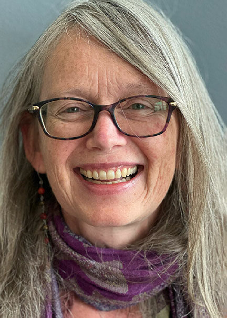 Rozalyn Anderson er professor i medisin. Middelaldrende kvinne som smiler bredt og ser inn i kameraet. Hun har langt, gråblondt hår, sideskill, mørk brilleinnfatning, blågrønne øyne og et lilla skjerf rundt halsen. Vi skimter en lang øredobb inne i håret.